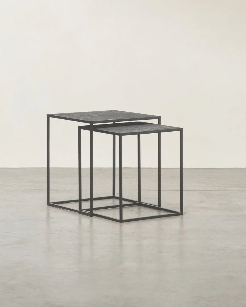 Set of two black nesting tables on a light wooden floor with a white wall background