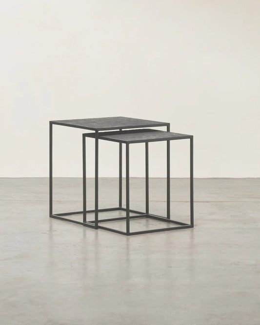 Set of two black nesting tables on a light wooden floor with a white wall background