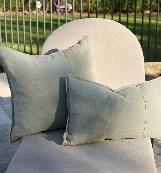 Two green pillows on a chair outdoors with grass and a fence in the background