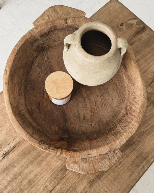 Wooden bowl with a ceramic pitcher and wooden lid on a wooden surface.