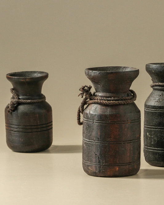 Three black ceramic pots with rope handles on a beige background